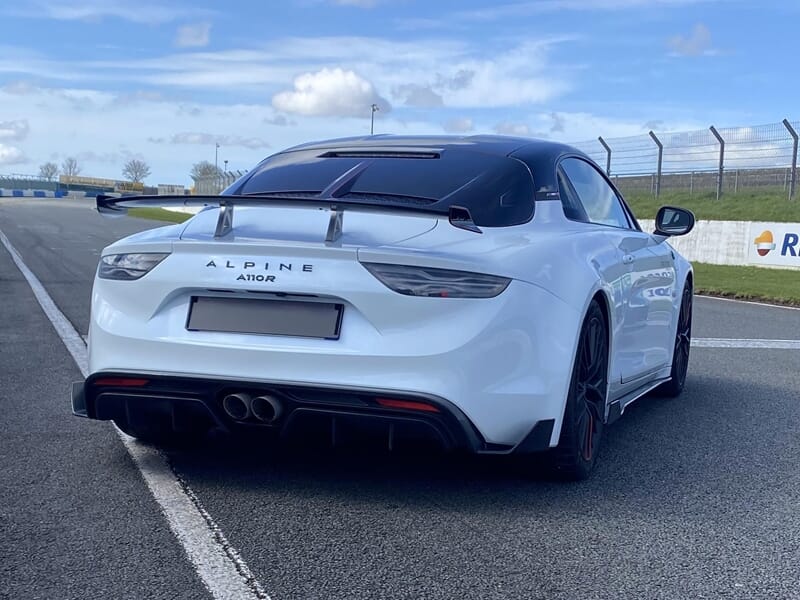 Vue arrière d’une Alpine A110R sur circuit, aileron relevé et échappement sport visible