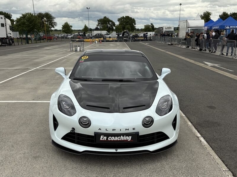 Voiture Alpine A110R blanche et noire sur circuit, vue de face avec capot carbone.