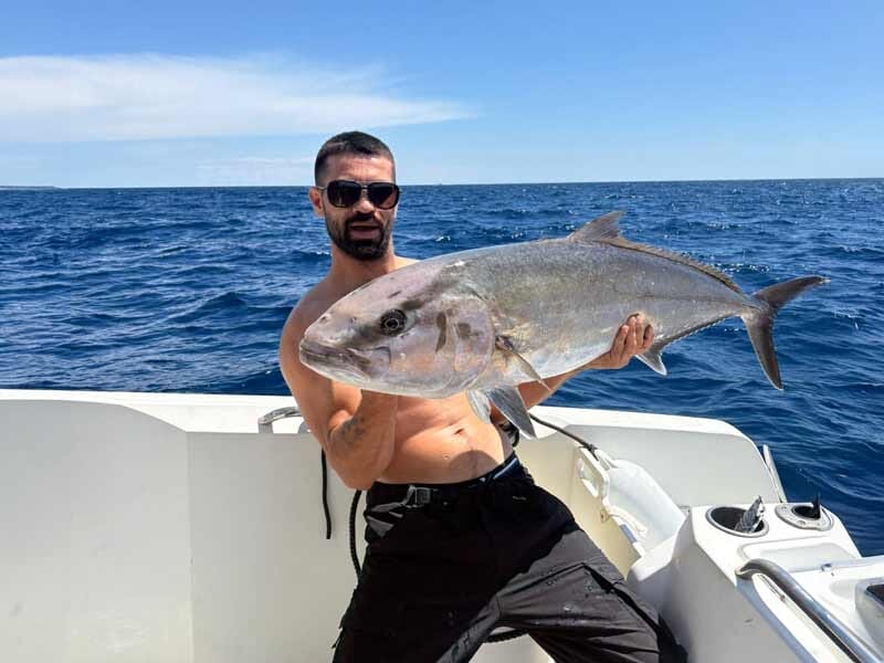 Homme sur un bateau tenant un gros poisson argenté pêché en mer Méditerranée à Mandelieu-La Napoule.