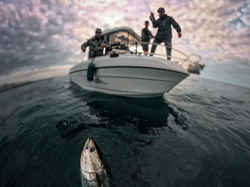 Poisson accroché à une ligne de pêche avec un bateau et trois pêcheurs en arrière-plan sur la mer.