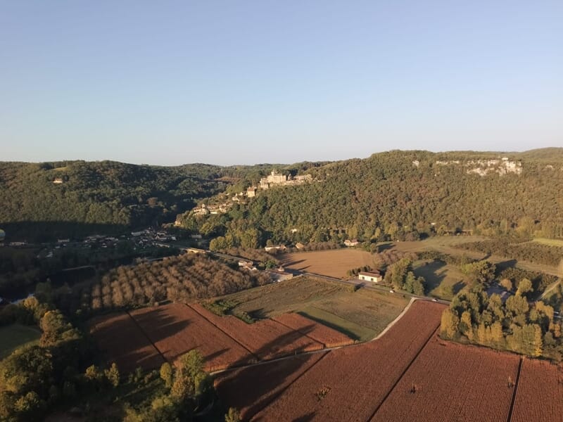 Champs cultivés et collines verdoyantes avec un château en arrière-plan au sommet de la colline.