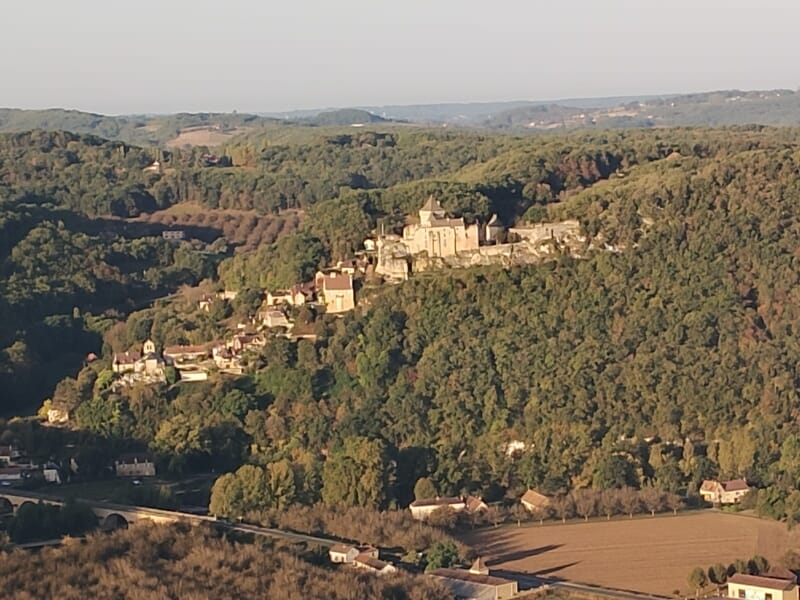 Vue aérienne d’un village médiéval perché sur une colline boisée avec son château dominant la vallée.