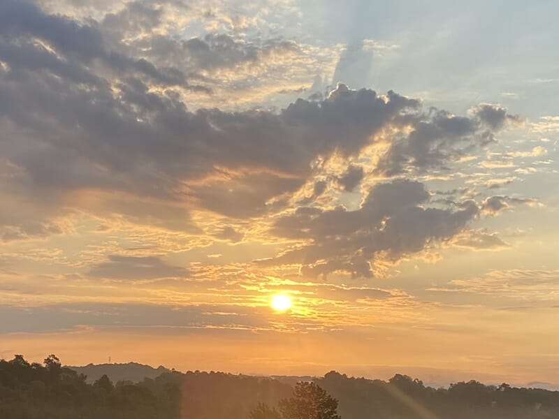 Ciel au coucher de soleil avec des nuages colorés en orange et or au-dessus des collines.