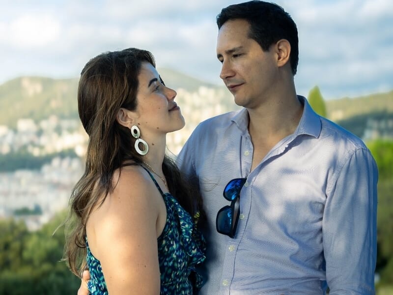 Un couple debout face à face, échangeant un regard affectueux avec une ville en arrière-plan.