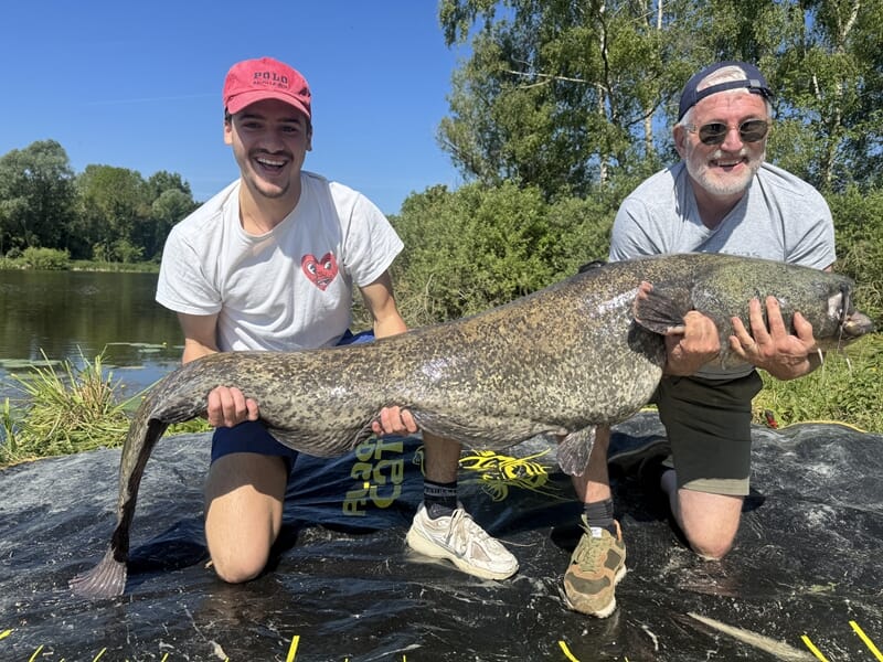 Deux pêcheurs montrant un silure impressionnant au bord de l’eau