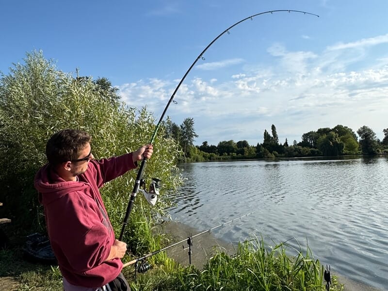 Pêcheur en action, canne à pêche courbée au bord d’un lac