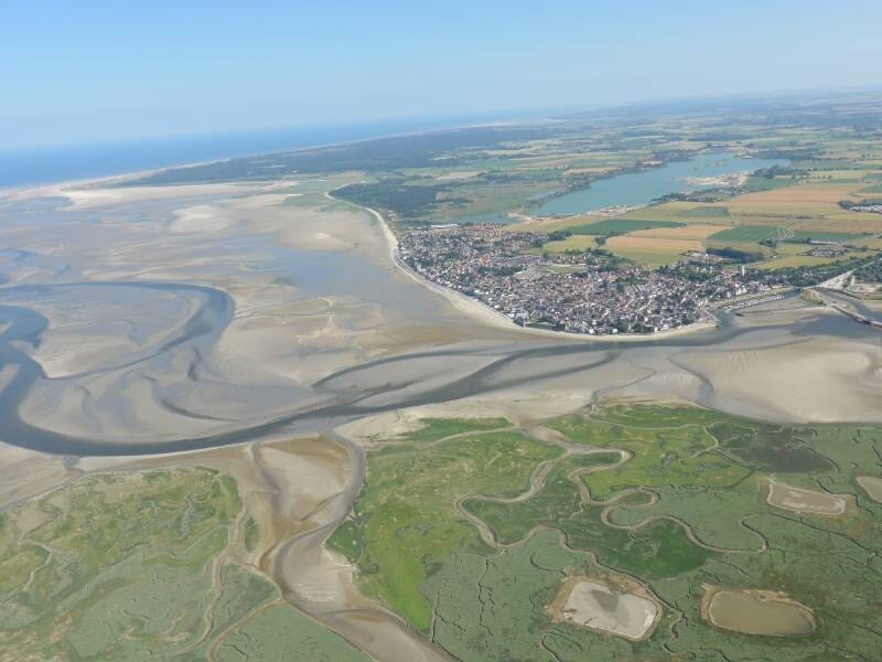 Vue aérienne sur les méandres de la baie de Somme et une ville qui les borde.