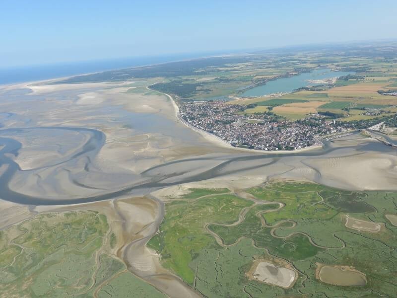Vue aérienne sur les méandres de la baie de Somme et une ville qui les borde.
