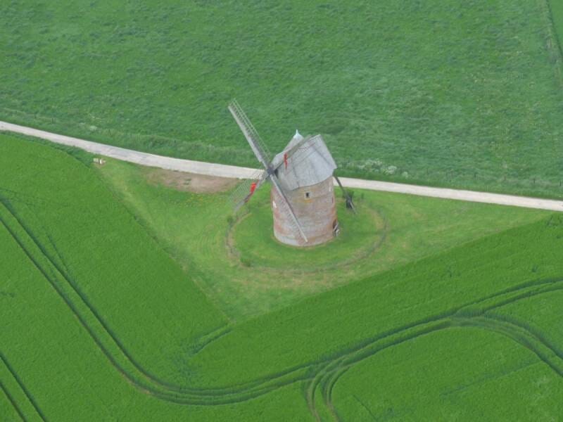 Vue aérienne sur un moulin construit au milieu des champs verdoyants.