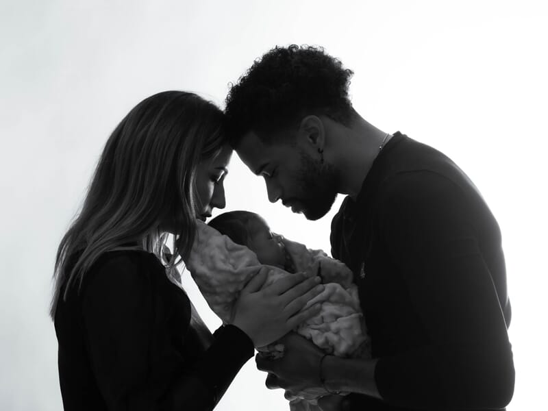 Portrait en contre-jour d’un couple serrant leur bébé dans les bras avec tendresse et émotion.