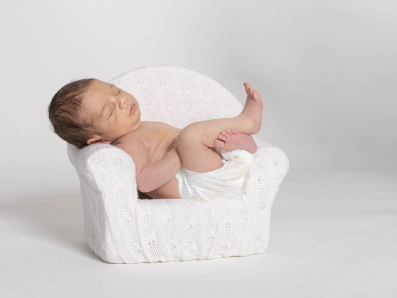 Nouveau-né endormi dans un petit fauteuil blanc en laine, capturé en studio sur fond clair.