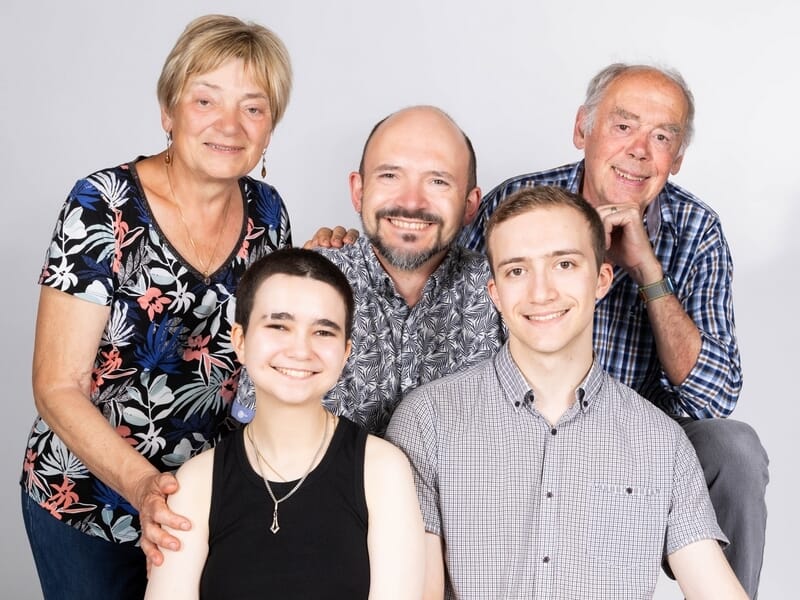 Portrait d’une famille de cinq personnes posant ensemble en studio, souriantes et habillées de façon décontractée.