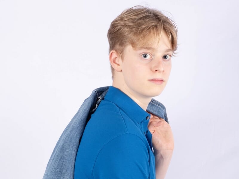 Jeune homme en chemise bleue, tenant une veste sur l’épaule, portrait en studio sur fond clair.