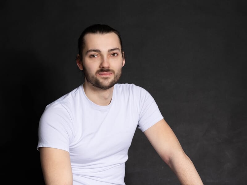 Jeune homme en t-shirt blanc assis devant un fond noir, regard vers l’objectif.