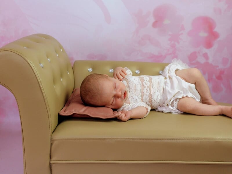 Nouveau-né dormant sur un petit canapé beige, image prise par une photographe bébé à Dijon.