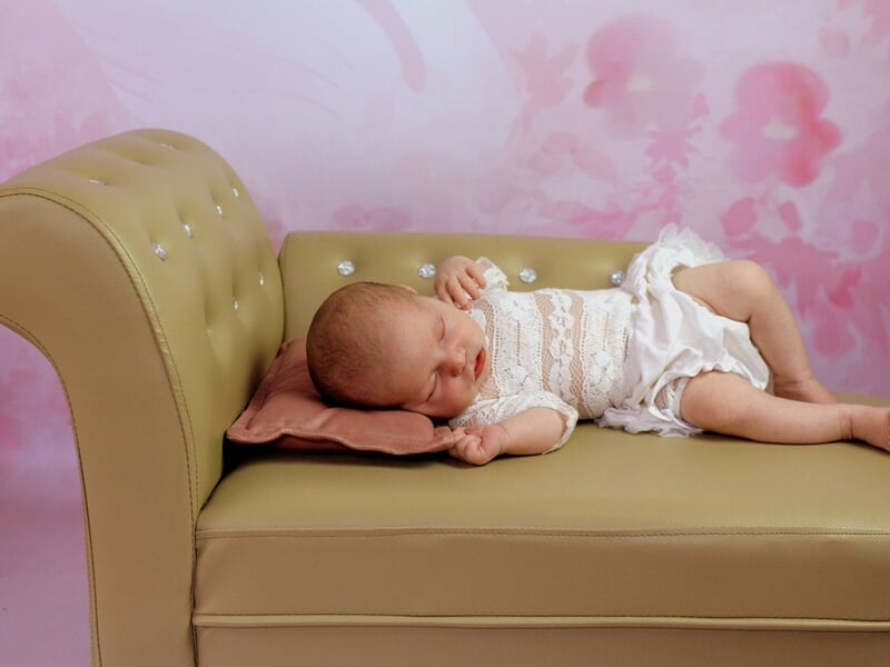 Nouveau-né dormant sur un petit canapé beige,  image prise par une photographe bébé à Dijon.