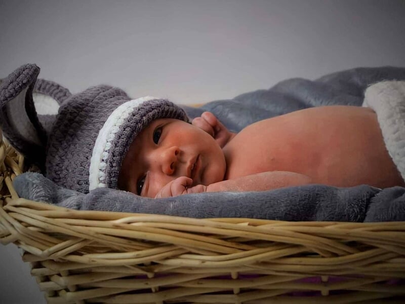 Bébé allongé dans un panier en osier, couvert d’une couverture grise et portant un bonnet tricoté,  image prise par une photographe bébé à Dijon