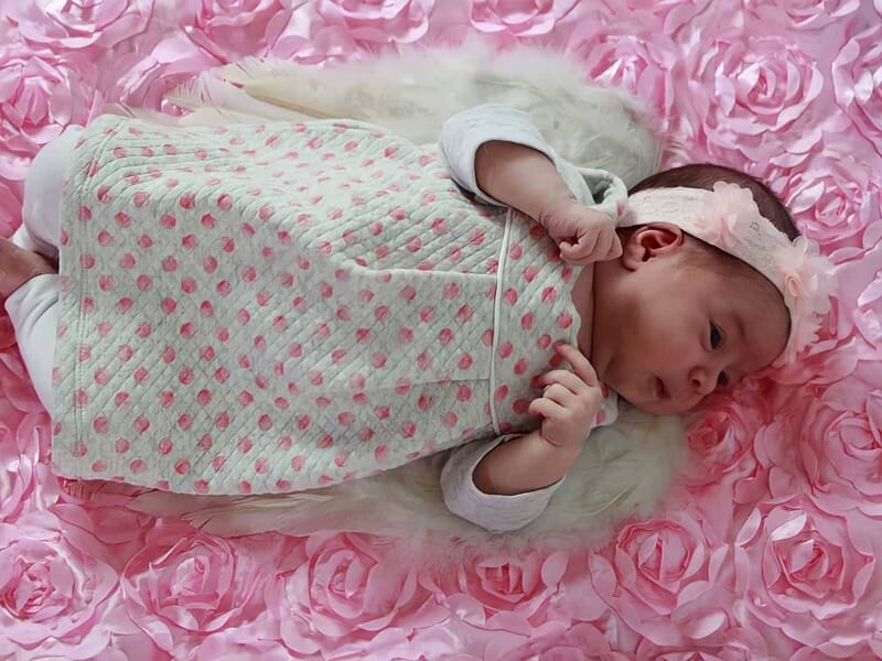Bébé allongé sur un tissu rose à motifs de fleurs, portant une robe claire à pois roses, image prise par une photographe bébé à Dijon