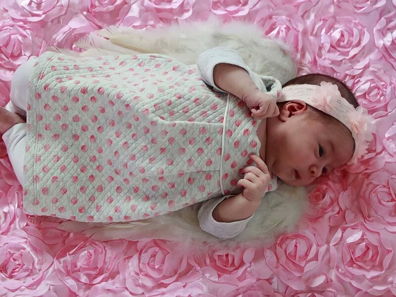 Bébé allongé sur un tissu rose à motifs de fleurs, portant une robe claire à pois roses,  image prise par une photographe bébé à Dijon
