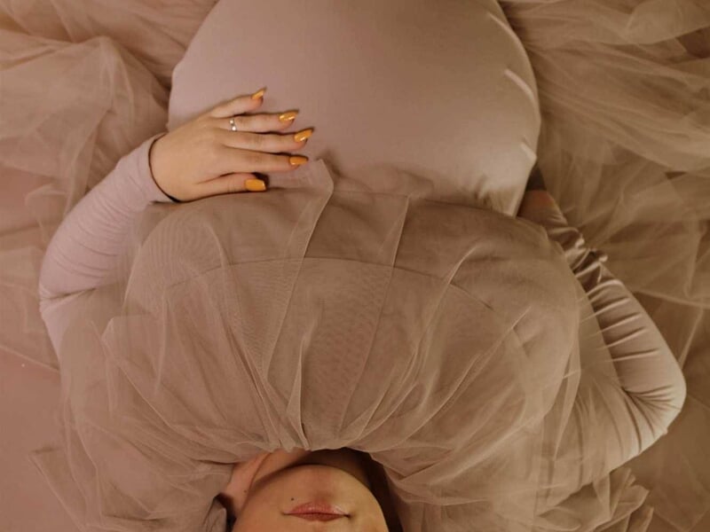 Future maman allongée en robe de tulle beige, image prise lors d'un shooting photo grossesse à Dijon