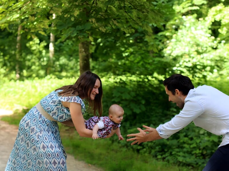 Séance photo famille Dijon en extérieur, parents jouant avec leur bébé dans la nature, moment complice et joyeux capturé en pleine verdure.