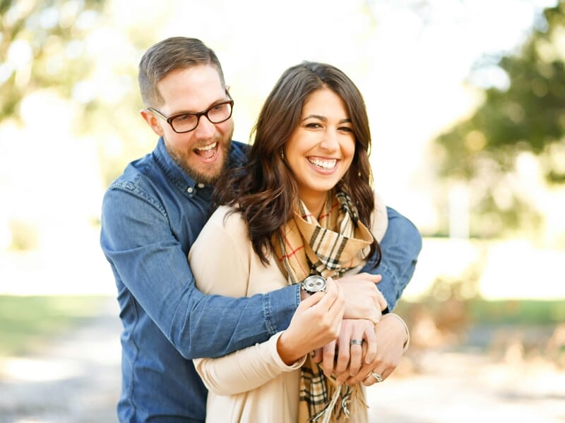 Shooting photo couple Dijon, homme barbu en chemise en jean enlac¸ant sa compagne souriante dans un parc.