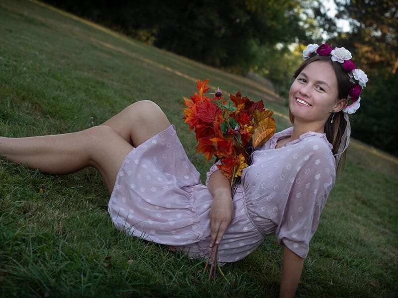 Photographe portrait Angers, jeune femme en robe rose pâle allongée dans l’herbe avec une couronne de fleurs et un bouquet automnal.