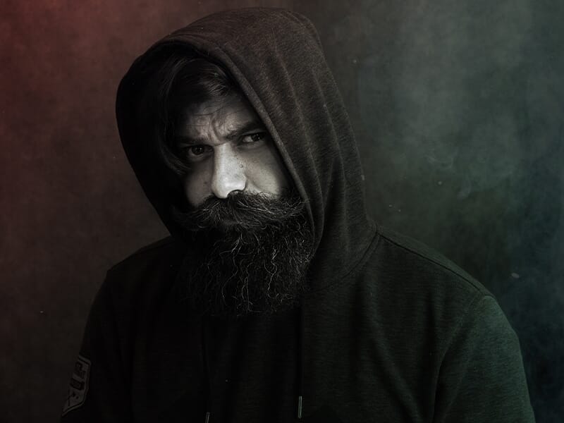 Photographe portrait Angers, homme barbu en sweat à capuche sombre, regard intense dans une ambiance artistique.