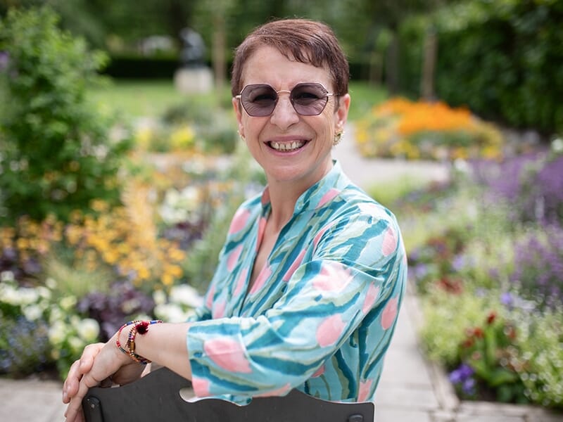 Photographe portrait Angers, femme souriante assise dans un jardin fleuri coloré, posant avec naturel et élégance.