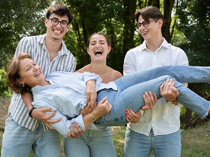 Quatre personnes souriantes dans un parc, trois jeunes hommes et une femme tenue en l'air, ambiance joyeuse et conviviale lors d'un shooting photo famille à Angers.