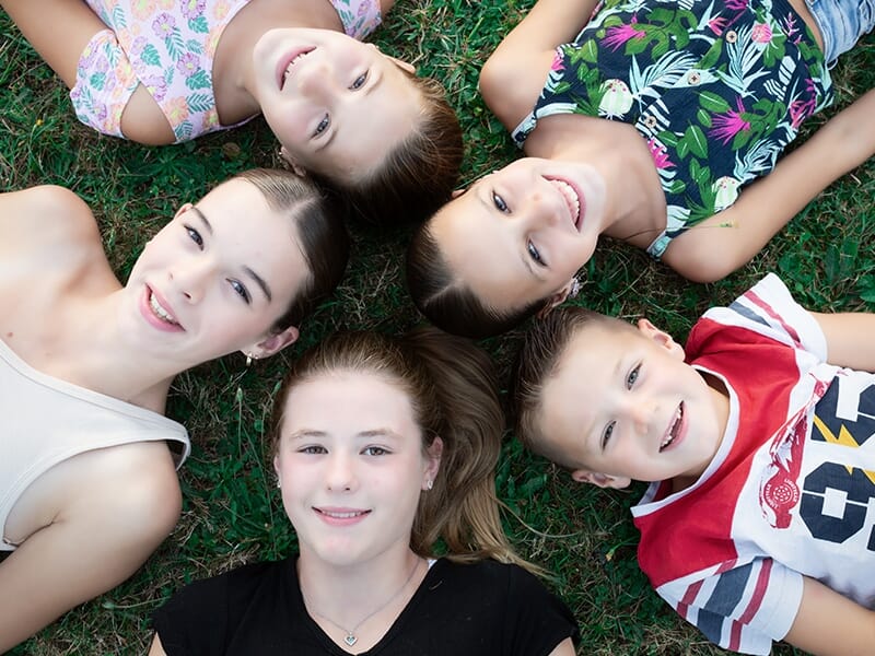 Cinq enfants allongés en cercle sur l'herbe, souriants et regardant vers le haut, ambiance estivale et amicale lors d'un shooting photo famille à Angers.