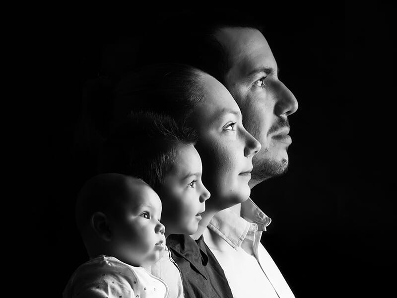 Portrait noir et blanc d'une famille de quatre personnes regardant vers la droite, avec un éclairage doux et un fond sombre lors d'un shooting photo famille à Angers.
