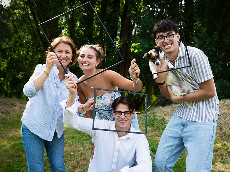 Quatre personnes dans un parc tenant des cadres vides, avec un petit chien, souriants et posant de façon ludique lors d'un shooting photo famille à Angers.
