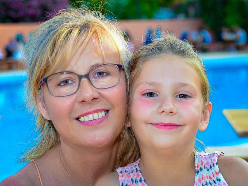 Portrait d'une femme souriante avec des lunettes et une jeune fille aux joues roses près d'une piscine en extérieur, lors d'une séance photo à Argelès.