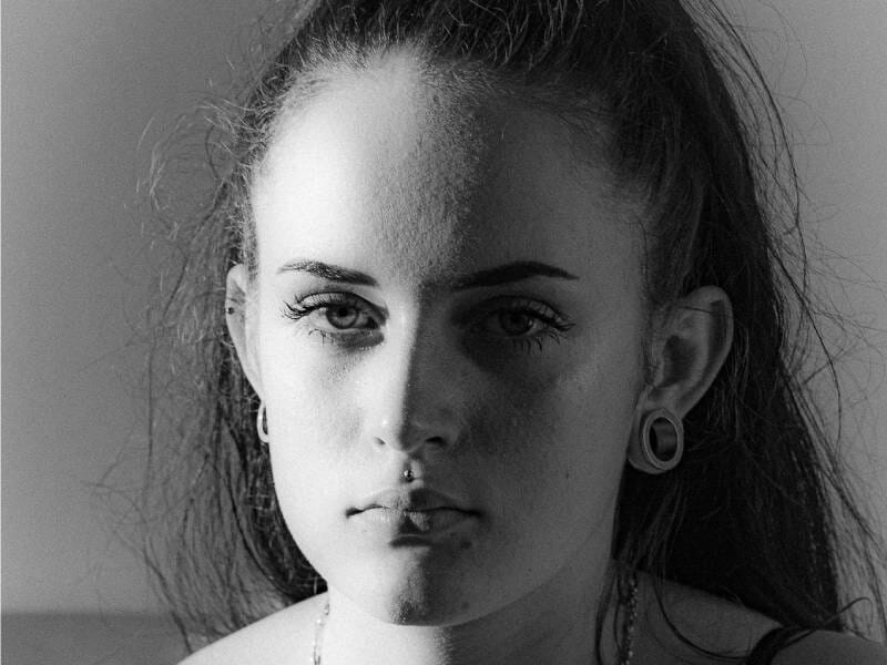 Portrait en noir et blanc d'une jeune femme au visage éclairé d'un côté, regard intense et cheveux attachés.