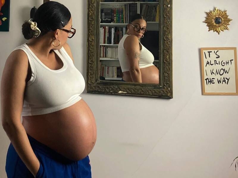Une femme enceinte pose devant un miroir et observe son reflet.