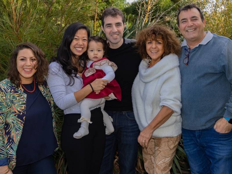 Trois femmes et deux hommes prennent la pose en famille, la femme du milieu tient un enfant dans ses bras.