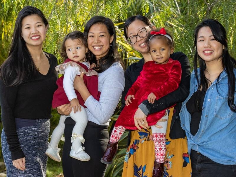 Quatre femmes prennent la pose, celles du milieu tiennent chacune un enfant dans leurs bras.