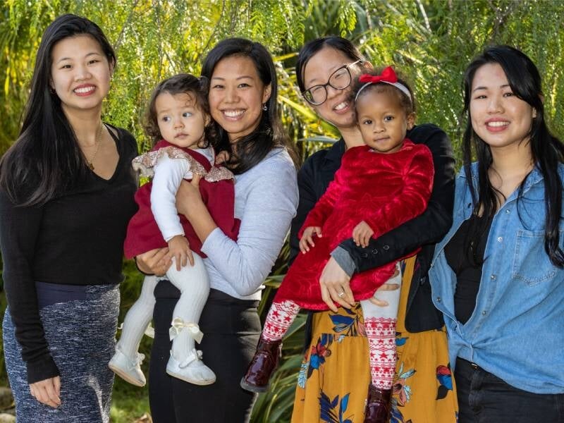 Quatre femmes prennent la pose, celles du milieu tiennent chacune un enfant dans leurs bras.
