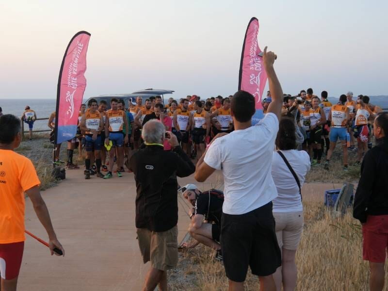 Groupe de coureurs rassemblés au départ d'une course en plein air au coucher du soleil, avec des drapeaux roses.