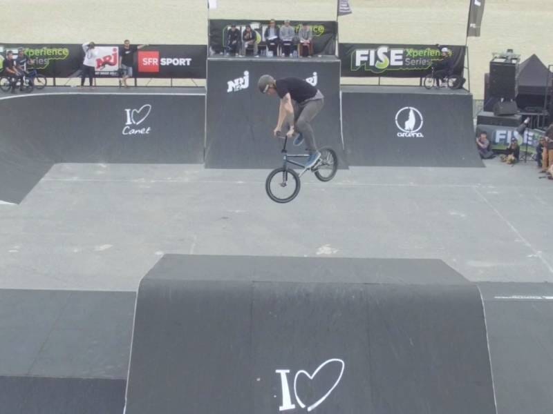 Un cycliste réalise un saut acrobatique en BMX sur une rampe dans un skatepark lors d'une compétition.