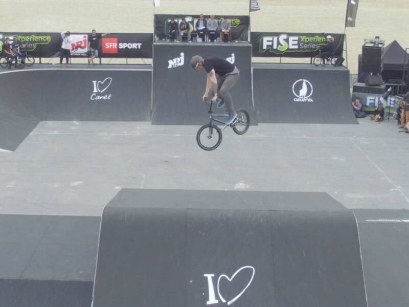 Un cycliste réalise un saut acrobatique en BMX sur une rampe dans un skatepark lors d'une compétition.