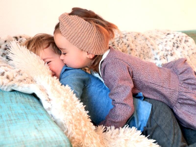 Deux jeunes enfants qui se font un câlin dans un canapé avec des plaids.