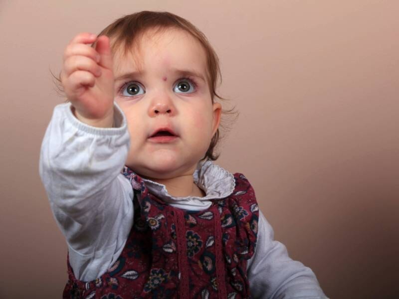 Un bébé qui semble intrigué et tend la main vers quelque chose.