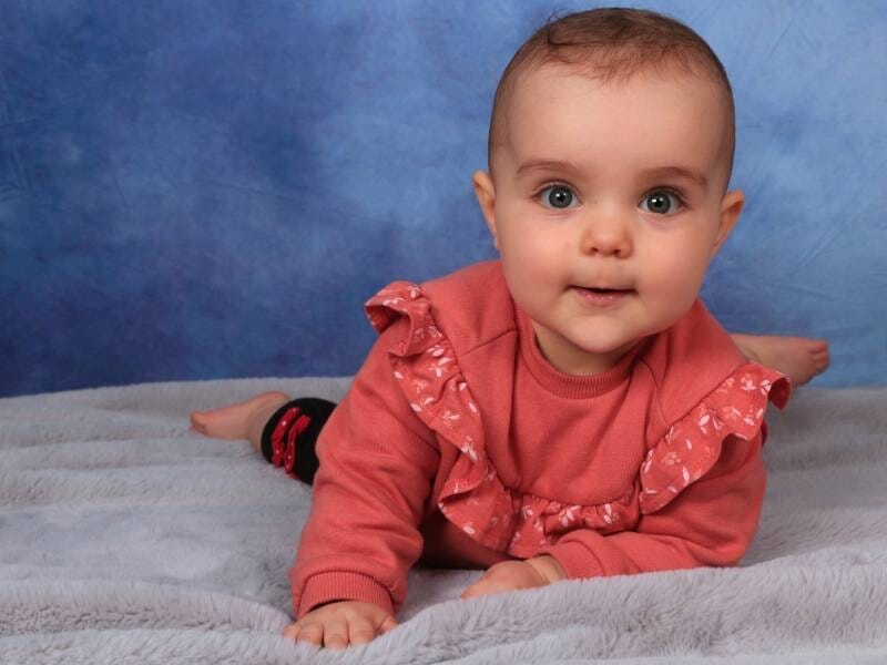 Un bébé allongé sur le ventre, habillé en rose, regarde l'objectif.