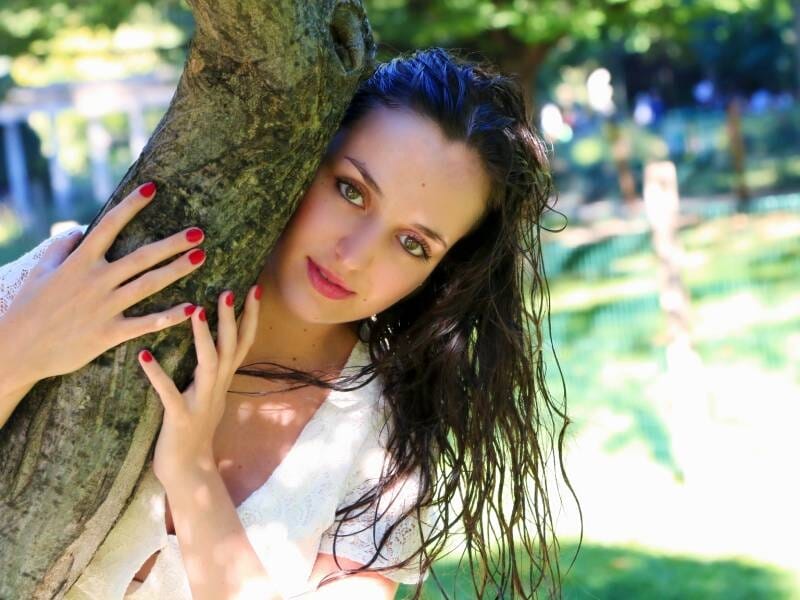 Une femme enlace un arbre et fixe l'objectif en prenant la pose.
