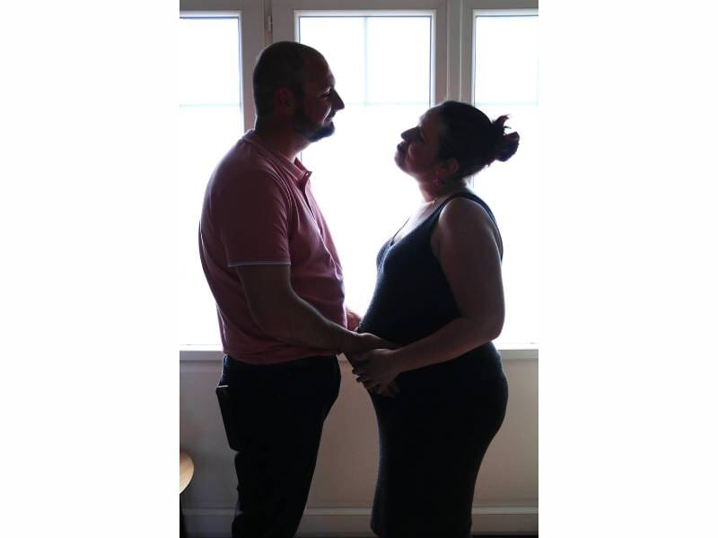 Un homme et une femme enceinte, face à face, se tiennent par les mains.