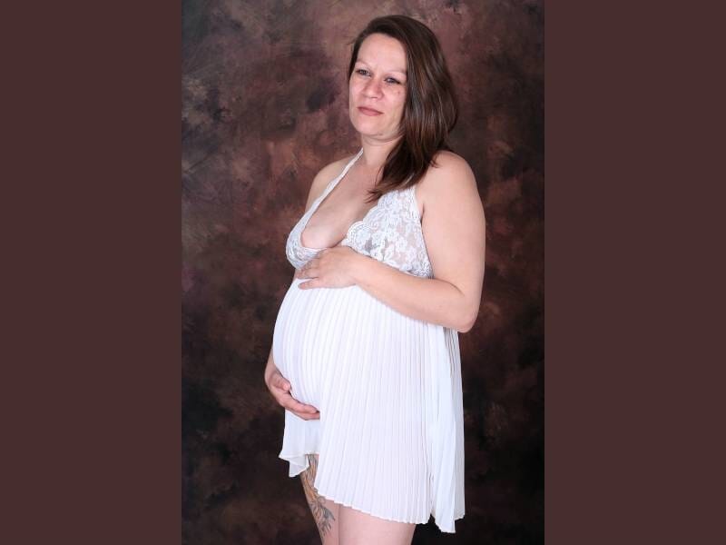 Une femme vêtue d'une robe blanche prend la pose, les mains posées sur son ventre rond.