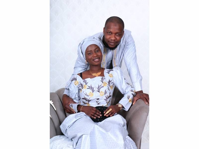 Un couple habillé en tenue traditionnelle africaine, assis et posant avec affection devant un fond clair.