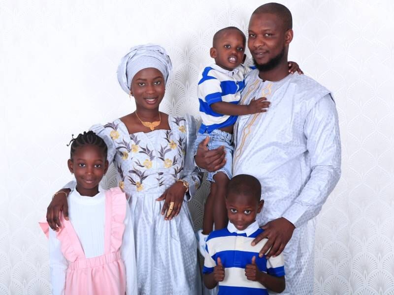 Portrait d'une famille africaine souriante avec deux enfants et un bébé, vêtus de tenues traditionnelles et modernes.
